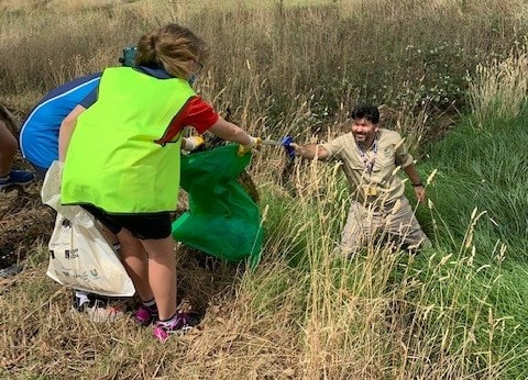 Photograph showing three people participating in an outdoor clean up activity in a grassy field.