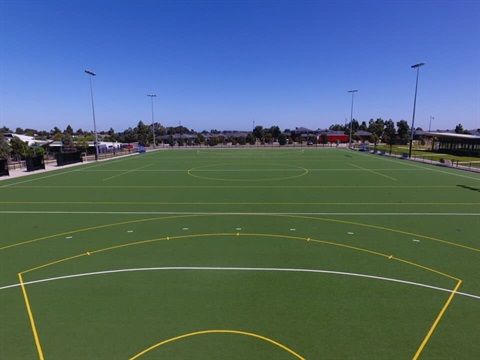 Wide-angle view of a green hockey pitch in Hume City with a clear blue sky. 